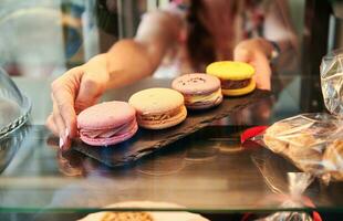 Nahansicht von ein Cafeteria Arbeiter nehmen bunt Macarons von ein Vitrine im Gebäck Geschäft foto