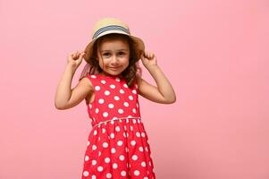 süß kaukasisch Baby Mädchen im Rosa Sommer- Kleid und Stroh Hut posieren Über Rosa Mauer Hintergrund mit Kopieren Raum. Studio Porträt von glücklich lächelnd bezaubernd Kind 3-4 Jahre. foto