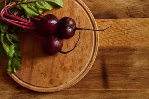 eben legen von ein Bündel von frisch Burgund Rote Beete mit Grün Spitzen und Blätter auf ein hölzern Schneiden Tafel . Essen Hintergrund von saisonal roh Gemüse foto