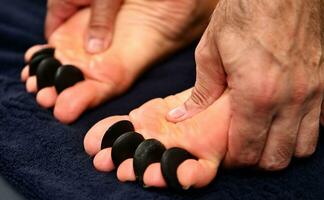 Nahansicht von ein Massage Therapeut durchführen ein ayurvedisch Akupressur auf das Füße mit heiß vulkanisch Steine. Spa Behandlung Konzepte foto
