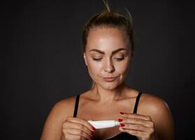 angenehm atemberaubend Mitte alt kaukasisch Frau Öffnung ein Tube mit Antialterung Feuchtigkeitscreme, Anti Falten Serum unter Augen. Schönheit Behandlung Konzept, Haut Pflege. foto