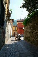 schön Mutter schieben ein Kinderwagen mit Schlafen Baby, Gehen entlang ein Kopfsteinpflaster Gasse im mittelalterlich Italienisch Gesang Stadt, Dorf foto