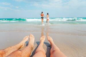 Nahansicht von das Füße von Familie auf das Weiß sandig Strand. Kinder abspielen auf das Strand im flach Wasser auf Sommer- Ferien foto