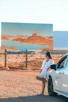 schön Frau auf ihr Ausflug durch das Auto auf das Hintergrund von herzlich willkommen zu Utah Zustand Rand Zeichen richtig im das Monument Senke foto