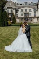 das Braut und Bräutigam Stand auf ein malerisch Feld auf das Hochzeit Tag auf das Hintergrund von ein wunderbar Wald und ein teuer Hotel foto