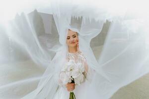 glücklich schön Braut unter Schleier Nahaufnahme. schön Braut zeigt an bilden und Frisur. Braut im ein Weiß Kleid Theaterstücke mit ihr Schleier. foto