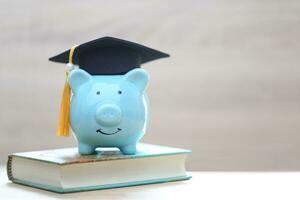 Abschluss Hut auf Schweinchen Bank und ein Bücher auf Weiß Hintergrund, Speichern Geld zum Bildung Konzept foto