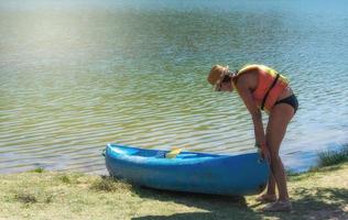 Frau in Schwimmweste schiebt Kanu ins Wasser foto