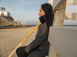 Mädchen mit zerzausten Haaren sitzt auf einem Holzdesign am Strand foto