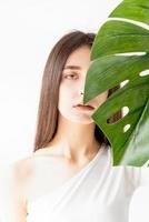 glückliche schöne Frau in gemütlicher Kleidung, die ein grünes Monstera-Blatt hält foto