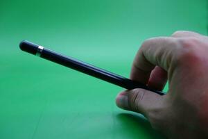 ein schwarz Stift Stift Sein gehaltenen Über ein Grün Hintergrund. foto