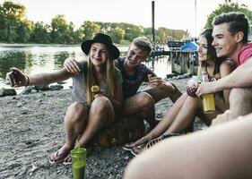 Gruppe von freunde Sitzung zusammen haben ein Grill und nehmen ein Selfie beim das Flussufer foto