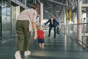 glücklich Kind Laufen in Waffen von Reisen Geschäftsmann beim das Flughafen foto