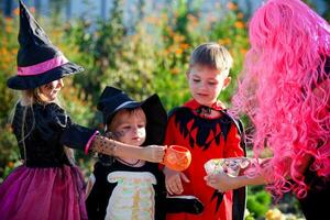 Gruppe Kinder Trick oder behandeln im Halloween Kostüm . ein wenig Jungs und ein Mädchen im Anzüge erhalten Süßigkeiten von ein Frau gekleidet . foto