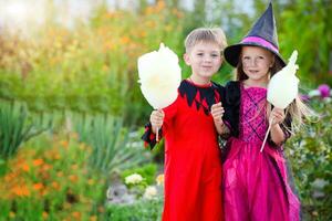 wenig Junge und Mädchen im Kostüme von ein Hexe und ein Henker zum Halloween. Kinder halten Baumwolle Süßigkeiten. foto