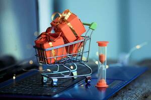 Sanduhr und klein Korb mit Kisten von Weihnachten Geschenke auf das Hintergrund von ein Laptop. online Einkaufen. Boxen Tag Konzept. haben Zeit zu besorgen. Verkauf. foto