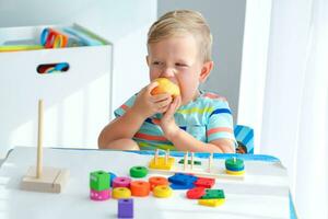 ein wenig Junge 2 Jahre isst ein Apfel und ist gespielt mit hölzern Bälle. lehrreich Logik Spielzeuge zum Kinder. montessori Spiele zum Kind Entwicklung. foto