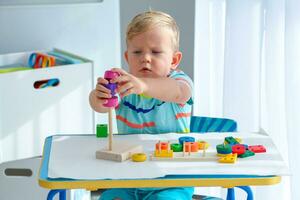 wenig Junge 2 Jahre alt ist gespielt mit ein hölzern Pyramide. lehrreich Logik Spielzeuge zum Kinder. montessori Spiele zum Kind Entwicklung. foto