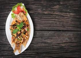 gebratener Fisch mit würzigem Salat im Teller auf Holztisch foto