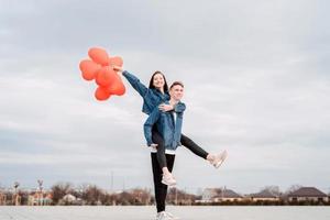 junges Liebespaar mit roten Luftballons, die sich im Freien umarmen und Spaß haben