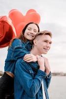 junges Liebespaar mit roten Luftballons, die sich im Freien umarmen foto