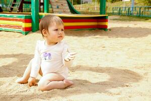 komisch Baby sitzt im das Sand auf das Spielplatz foto