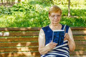 Senior Frau im das Park auf ein Bank lesen ein Buch foto