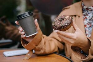 weiblich Hände sind halten ein Krapfen und ein Tasse von Kaffee foto