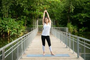 jung weiblich auf ein hölzern Brücke im das Park mit gesund Yoga Aktivitäten foto