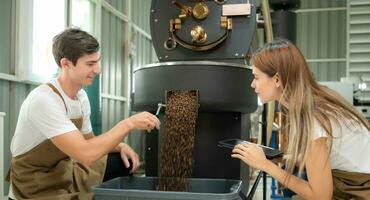 jung Mann und Frau Arbeiten im Kaffee Bohnen Bräter, Sie sind Überprüfung von Kaffee Bohnen geröstet. foto