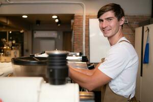 Porträt von ein jung männlich Barista vorbereiten Kaffee im ein Kaffee Geschäft foto