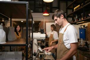 Porträt von ein jung männlich Barista im Schürze mit Zahlung Maschine im Cafe foto