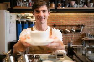 Porträt von ein lächelnd männlich Barista halten ein Tasse von Kaffee foto