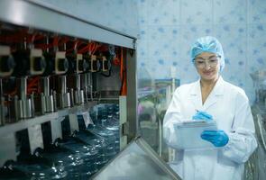 weiblich Wissenschaftler im Weiß Mantel und Blau Hut Arbeiten im das Steuerung Maschine von Produktion Linie. foto