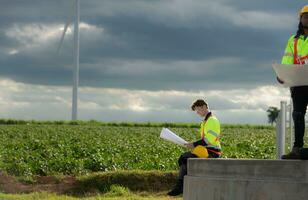 Ingenieure und Techniker Arbeit zusammen auf das Turm Base von ein groß Wind Turbine mit ein Wind Turbine Feld im das Hintergrund, das Konzept von natürlich Energie von Wind. foto