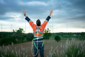 jung Ingenieur Arbeiten im ein Wind Turbine Feld tragen ein Sicherheit Weste erziehen beide Hände zu entspannen nach Fertigstellung das Wind Turbine Inspektion Mission foto