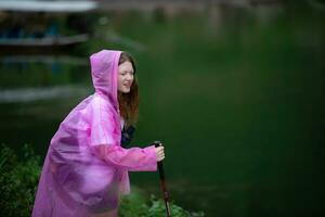 Mädchen im Regenjacke mit Gehen Stock auf das Hintergrund von das See foto