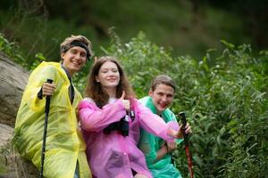 Gruppe von freunde im Regenmäntel mit Rucksäcke auf ein Wanderung im das Wald, bereiten zu Wandern nach das Regen hat gestoppt. foto