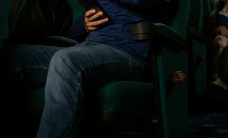 jung Mann Sitzung im ein Stuhl und mit seine Handy, Mobiltelefon Telefon im das Kino foto