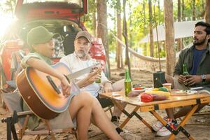 Gruppentouristen trinken Bieralkohol und spielen Gitarre zusammen mit Spaß und Glück im Sommer beim Camping foto