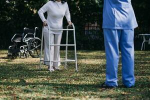 asiatisch jung Frau Krankenschwester beim Pflege- Zuhause nehmen Pflege deaktiviert Senior Mann. Pflegekraft Arzt Dienen physisch Therapie zum älter Alten geduldig zu Übung und trainieren Gehen auf Gehhilfe oder Stock beim Hinterhof. foto