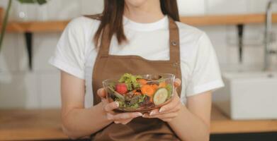 köstlich Obst und Gemüse auf ein Tabelle und Frau Kochen. Hausfrau ist Schneiden Grün Gurken auf ein hölzern Tafel zum Herstellung frisch Salat im das Küche. foto
