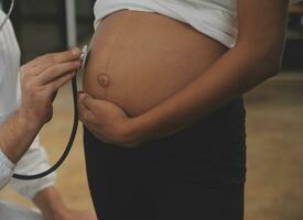 weiblich Arzt ist Überprüfung schwanger Frau mit Stethoskop. Konzept Pflege zum schwanger Frau foto