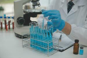 Wissenschaftler oder medizinisch im Labor Mantel Arbeiten im biotechnologische Labor, Mikroskop Ausrüstung zum Forschung mit Mischen Reagenzien im Glas Flasche im klinisch Labor. foto