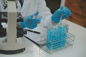 Wissenschaftler oder medizinisch im Labor Mantel Arbeiten im biotechnologische Labor, Mikroskop Ausrüstung zum Forschung mit Mischen Reagenzien im Glas Flasche im klinisch Labor. foto