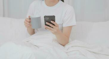 effizient jung tausendjährig Mädchen Sitzung auf ein Bett im das Morgen, Verwendet Laptop Computer und isst Croissants und Getränke Kaffee zum Frühstück foto