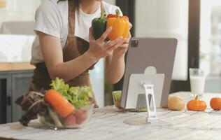 köstlich Obst und Gemüse auf ein Tabelle und Frau Kochen. Hausfrau ist Schneiden Grün Gurken auf ein hölzern Tafel zum Herstellung frisch Salat im das Küche. foto
