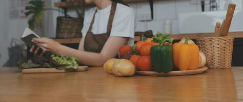 köstlich Obst und Gemüse auf ein Tabelle und Frau Kochen. Hausfrau ist Schneiden Grün Gurken auf ein hölzern Tafel zum Herstellung frisch Salat im das Küche. foto