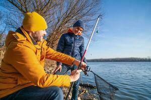 Vater und Sohn sind Angeln auf sonnig Winter Tag. frisches Wasser Angeln. Teenager Junge ist Lernen zu Fisch. foto