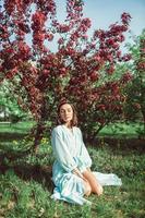 Mädchen sitzt im Park auf dem Gras unter einem blühenden weißen Apfelbaum foto